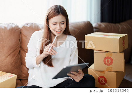 Starting small business entrepreneur of independent young Asian woman online seller is using tablet computer and taking orders to pack products for delivery to customers. SME delivery concept. Starting small business entrepreneur of independent young Asian woman online seller is using tablet computer and taking orders to pack products for delivery to customers. SME delivery concept. 103318346