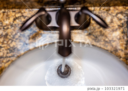 Top down view above a bathroom faucet with water pouring into the sink.  103321971
