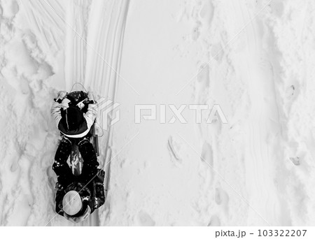 Aerial overhead done photo of two children in a sled going down a snow covered hill.  103322207