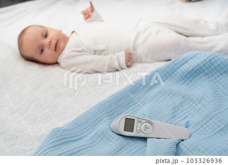 A non-contact thermometer and a newborn baby in the background as a concept for a modern temperature measurement method A non-contact thermometer and a newborn baby in the background as a concept for a modern temperature measurement method 103326936