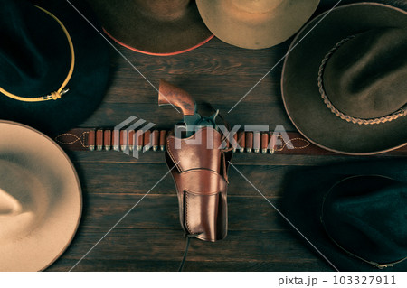 Gun with holster and gunbelt with old west hats on table. Top view. Gun with holster and gunbelt with old west hats on table. Top view. 103327911