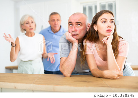 Husband and wife listen to their parents scold them in home kitchen Husband and wife listen to their parents scold them in home kitchen 103328248