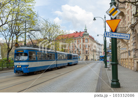 【ポーランド】クラクフ旧市街の伝統的な街並みの中を走り抜ける近代的な青色のトラム 103332086
