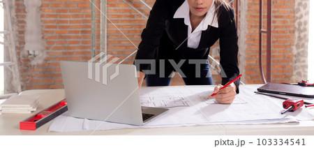 Young caucasian architect woman looking laptop and working drawing blueprint for planning building. 103334541