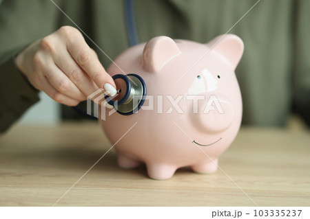 Female person checks piggy bank condition with stethoscope Female person checks piggy bank condition with stethoscope 103335237