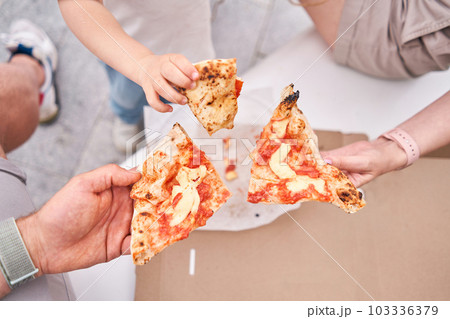 Family lunch. Dad, mom and daughter had a pizza picnic in the park. Pizza delivery concept in a cardboard box. Baked a delicious pizza Margarita in a traditional wood-burning oven in a Neapolitan 103336379
