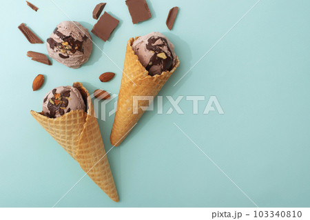 Chocolate ice cream in a waffle cone, blue background, flat lay, top view, copy space. Summer cooling desserts Chocolate ice cream in a waffle cone, blue background, flat lay, top view, copy space. Summer cooling desserts 103340810