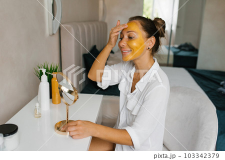 Caucasian woman apply a moisturizing golden mask on her face, facial skin care and spa treatments at home 103342379