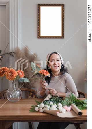 Startup, small business, flower shop. Older florist putting a flower on a vase 103343072