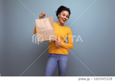 pretty positive20s latin woman with afro hair in casual yellow sweater holding purchase in kraftomo pretty positive20s latin woman with afro hair in casual yellow sweater holding purchase in kraftomo 103345529