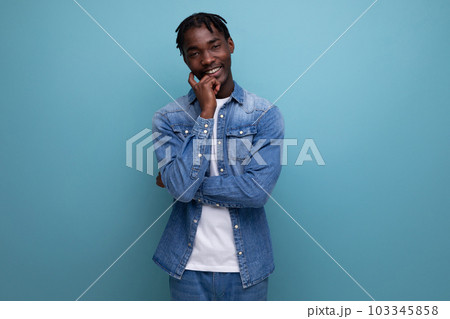 pensive brunette man with dreadlocks in a denim jacket on a blue background 103345858