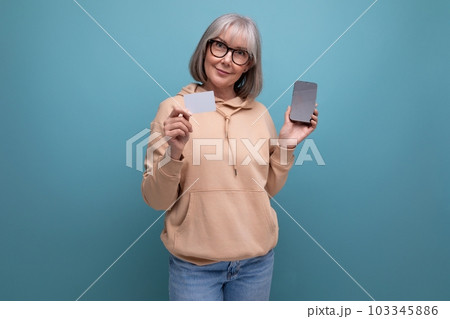 60s granny woman with gray hair keeps her savings on a credit card on a studio background with copy 103345886