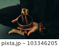 Top view of two hands of a man holding a singing bowl with sticks in front of him. Listen to the healing vibrations of Tibetan bowls. Humility and calm. Rosary on the hand. Close-up 103346205