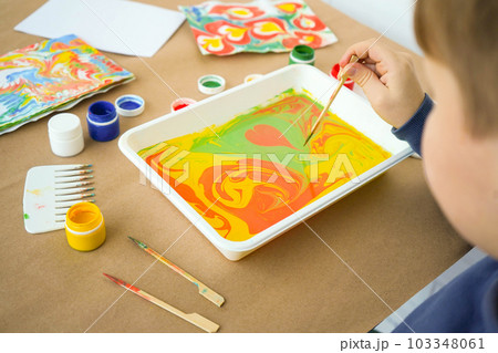 Boy is drawing Ebru and set of tools on table. Traditional Turkish Ebru technique. top view. Children development concept Boy is drawing Ebru and set of tools on table. Traditional Turkish Ebru technique. top view. Children development concept 103348061
