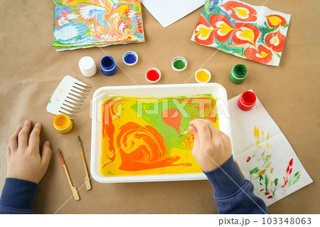 Boy is drawing Ebru and set of tools on table. Traditional Turkish Ebru technique. top view. Children development concept Boy is drawing Ebru and set of tools on table. Traditional Turkish Ebru technique. top view. Children development concept 103348063