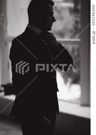 Silhouette of stylish groom stand in front of big window. Groom's morning Silhouette of stylish groom stand in front of big window. Groom's morning 103348300