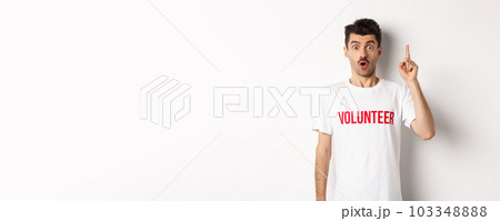 Handsome young man in volunteer t-shirt having an idea, raising finger and saying suggestion, pointing up, standing over white background Handsome young man in volunteer t-shirt having an idea, raising finger and saying suggestion, pointing up, standing over white background 103348888