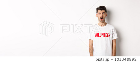 Shocked and confused man in volunteer t-shirt staring at camera speechless, standing against white background Shocked and confused man in volunteer t-shirt staring at camera speechless, standing against white background 103348995