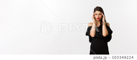 Fashion and beauty. Young modern woman in black dress, red lipstick, having headache, touching head and feeling sick, standing over white background 103349224