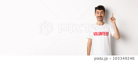 Handsome young man in volunteer t-shirt having an idea, raising finger and saying suggestion, pointing up, standing over white background Handsome young man in volunteer t-shirt having an idea, raising finger and saying suggestion, pointing up, standing over white background 103349246