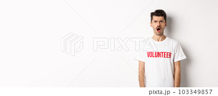 Shocked and confused man in volunteer t-shirt staring at camera and frowning displeased, standing against white background Shocked and confused man in volunteer t-shirt staring at camera and frowning displeased, standing against white background 103349857