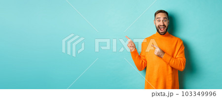 Excited man showing amazing promo offer, pointing fingers left at copy space on turquoise background 103349996