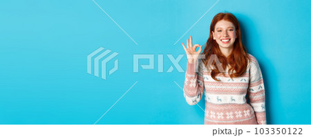 Cute smiling redhead woman showing okay sign, praising good work, well done gesture, standing over blue background Cute smiling redhead woman showing okay sign, praising good work, well done gesture, standing over blue background 103350122