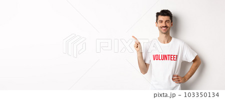 Handsome smiling volunteer in t-shirt pointing finger left, showing announcement, standing over white background Handsome smiling volunteer in t-shirt pointing finger left, showing announcement, standing over white background 103350134