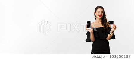 Fashion and shopping concept. Beautiful woman with red lips, winking at camera, showing smartphone screen and credit card, buying online, white background Fashion and shopping concept. Beautiful woman with red lips, winking at camera, showing smartphone screen and credit card, buying online, white background 103350187