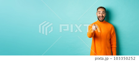Surprised man stare happy and pointing at camera, recognize someone, excited about seeing something, standing over light blue background Surprised man stare happy and pointing at camera, recognize someone, excited about seeing something, standing over light blue background 103350252