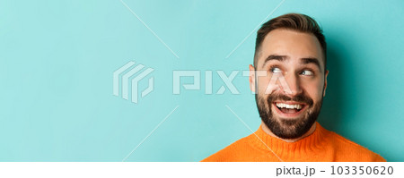 Headshot of handsome caucasian man looking at upper left corner logo and smiling pleased, checking out promo offer, standing over turquoise background 103350620