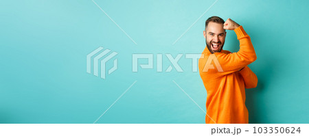 Confident handsome man show-off his muscles, flex biceps, feeling strong, standing over light blue background 103350624