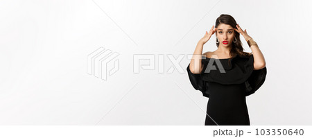 Fashion and beauty. Annoyed and tired woman in black dress, touching head and roll eyes bothered, standing distressed against white background Fashion and beauty. Annoyed and tired woman in black dress, touching head and roll eyes bothered, standing distressed against white background 103350640