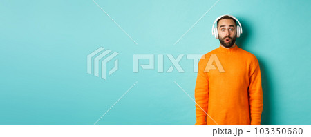 Amazed adult man listening music in headphones, looking at camera impressed with sound, standing over turquoise background Amazed adult man listening music in headphones, looking at camera impressed with sound, standing over turquoise background 103350680