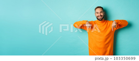 Happy adult man with beard pointing fingers down, smiling cheerful, showing advertisement, standing over turquoise background 103350699