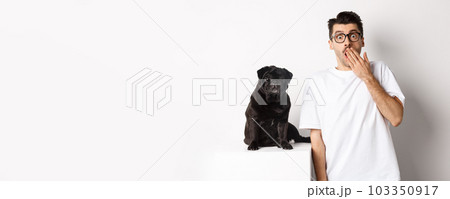 Image of dog owner and cute black pug looking at camera surprised and amazed, standing over white background Image of dog owner and cute black pug looking at camera surprised and amazed, standing over white background 103350917