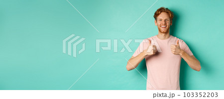 Cheerful bearded man with red hair showing thumbs-up, like and approve something, praising promo, standing against turquoise background Cheerful bearded man with red hair showing thumbs-up, like and approve something, praising promo, standing against turquoise background 103352203