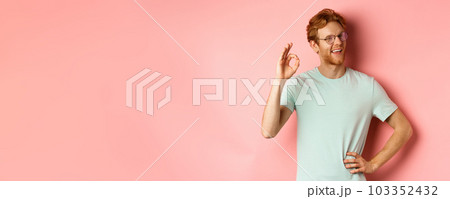 Cheerful guy with red hair and beard, wearing glasses, showing OK sign in approval and winking, smiling satisfied, standing over pink background Cheerful guy with red hair and beard, wearing glasses, showing OK sign in approval and winking, smiling satisfied, standing over pink background 103352432