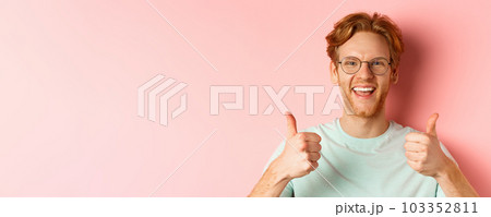 Face of satisfied male customer showing thumbs-up in approval, smiling happy, wearing glasses and t-shirt, pink background Face of satisfied male customer showing thumbs-up in approval, smiling happy, wearing glasses and t-shirt, pink background 103352811