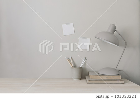 Wooden desk with lamp, books and cup holder for pencils. Note pad mockups taped on wall. Neutral stylish minimal workspace. Beige background, empty copy space. Home office concept, lifestyle banner. Wooden desk with lamp, books and cup holder for pencils. Note pad mockups taped on wall. Neutral stylish minimal workspace. Beige background, empty copy space. Home office concept, lifestyle banner. 103353221