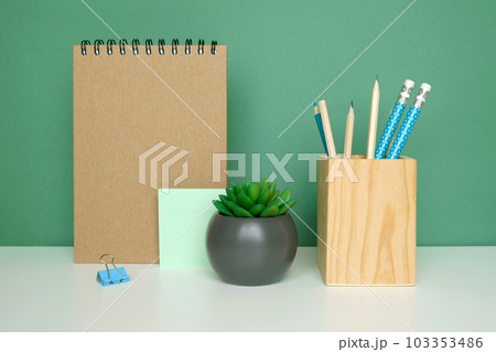 School equipment on white table, green wall background. Education backdrop. Wooden school supplies, notepad, pencils and cactus plant. Back to school. Student Desk. Stationery for study. Work at home School equipment on white table, green wall background. Education backdrop. Wooden school supplies, notepad, pencils and cactus plant. Back to school. Student Desk. Stationery for study. Work at home 103353486