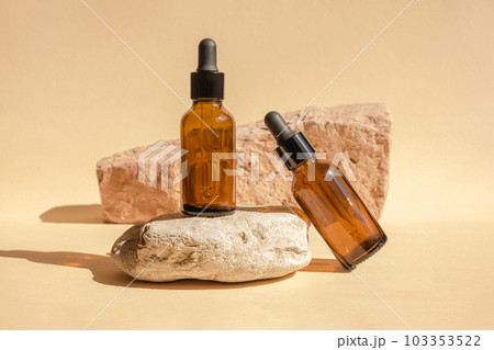 Dark amber glass bottle standing on stone. Natural skin care SPA beauty product design. Mineral organic oil cosmetics on beige background. Mock-Up. Dark amber glass bottle standing on stone. Natural skin care SPA beauty product design. Mineral organic oil cosmetics on beige background. Mock-Up. 103353522