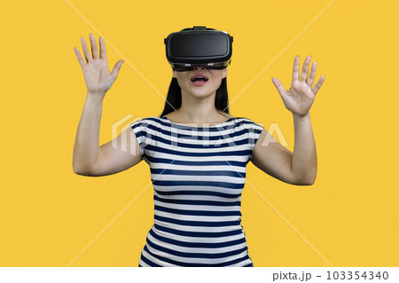 Portrait of a happy young smiling woman in vr headset with her hands up. Isolated on yellow. 103354340