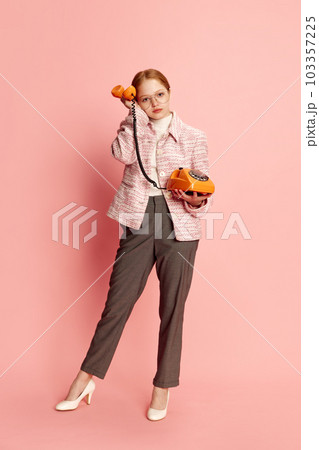 Busy woman, office worker wearing costume, eyeglasses and heels holding telephone receiver with an exhausted face on pink background. Concept of business, career 103357225