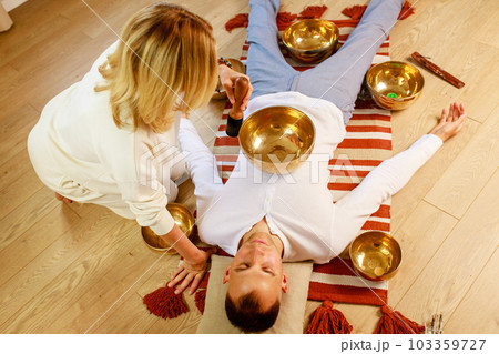 Woman playing on a tibetian singing bowl maling massage meditation for a man Woman playing on a tibetian singing bowl maling massage meditation for a man 103359727