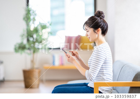 リビングでスマートフォンを操作する若い女性。 リビングでスマートフォンを操作する若い女性。 103359837