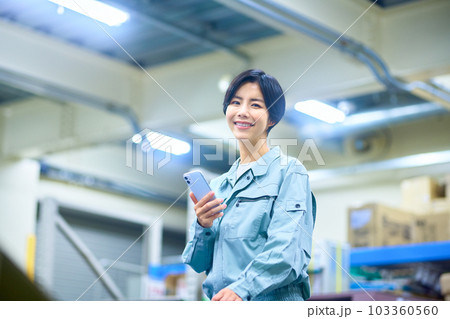 倉庫でスマホを操作する作業着の女性ビジネスマン 倉庫でスマホを操作する作業着の女性ビジネスマン 103360560