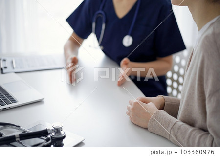 Doctor and patient sitting at the table in clinic while discussing something. The focus is on female patient's hands, close up. Medicine concept 103360976