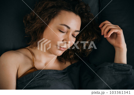A woman sleeps on her back on a bed at home 103361341