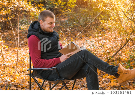 Young man is sitting on chair in an autumn park or Young man is sitting on chair in an autumn park or 103361461
